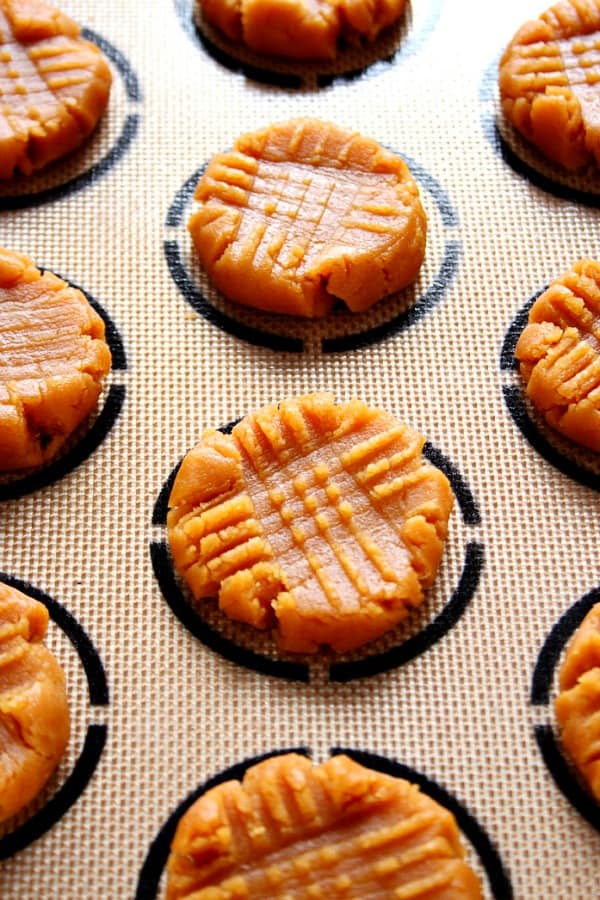 Side shot of peanut butter cookie dough, flattened on silicone baking mat.