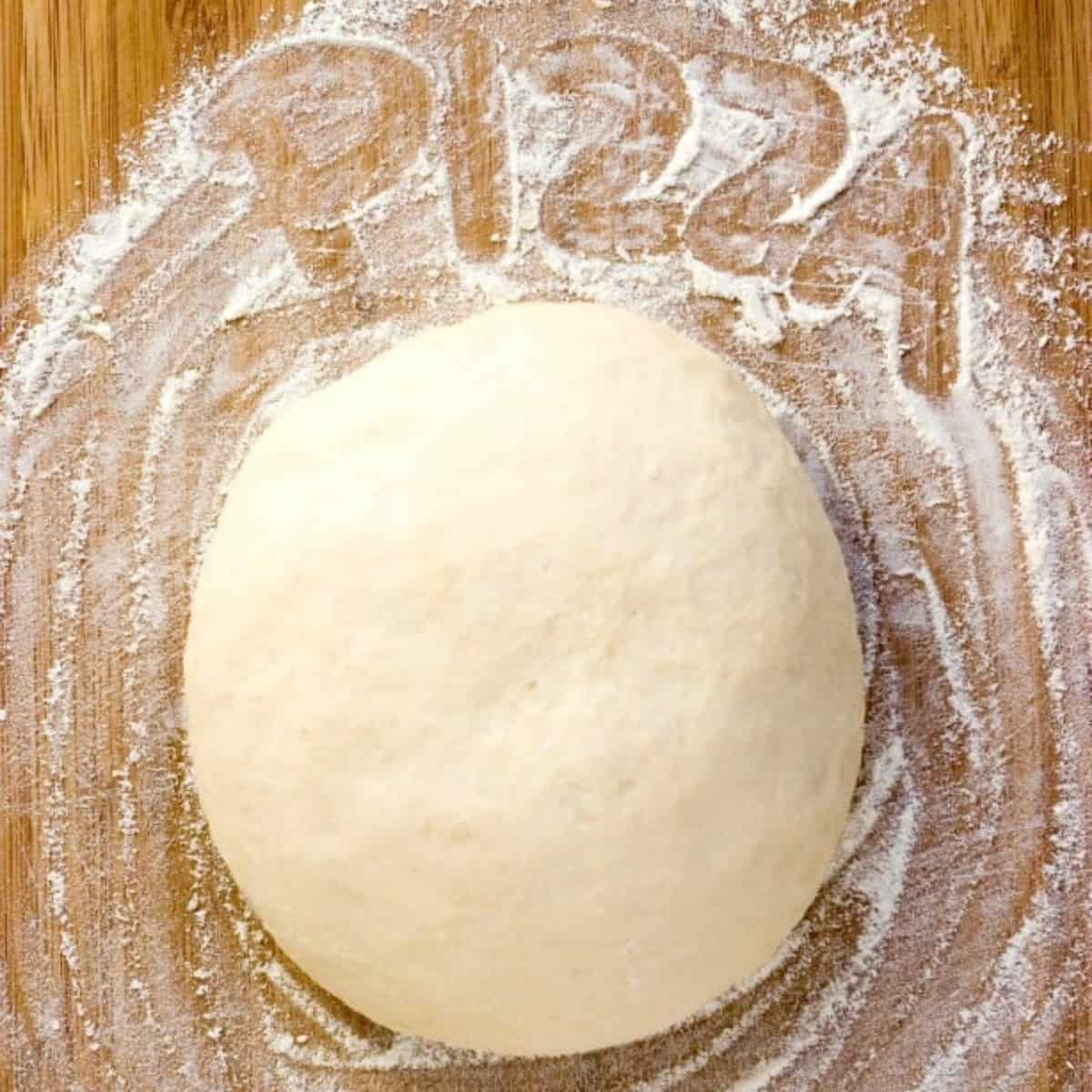 Ball of pizza dough on floured surface.