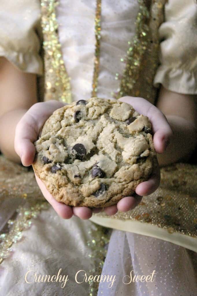 A girl in princess dress holding a chocolate chip cookie in hands.