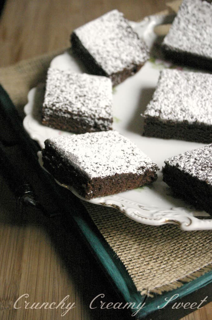 Side shot of brownies with powdered sugar on plate.