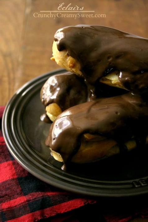 Side shot of eclairs stacked on each other on brown plate.