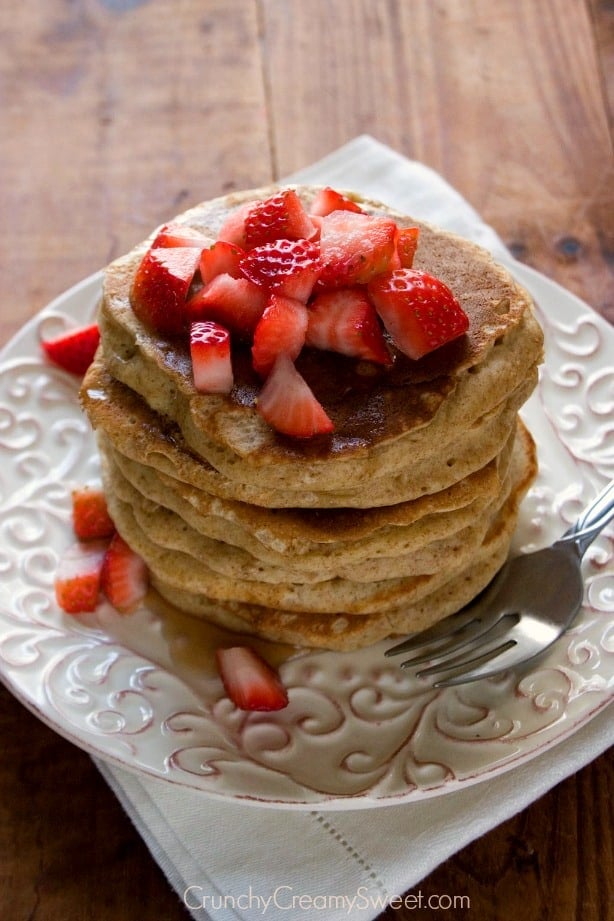 Overhead shot of a stack of whole wheat pancakes with chopped strawberries on top.