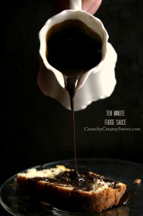 Side shot of fudge sauce being poured from a container onto a piece of cake.