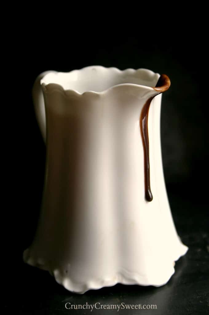 Side shot of hot fudge sauce dripping from a serving cup.