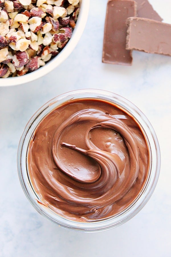 Homemade Nutella in jar, hazelnuts in a bowl next to it.