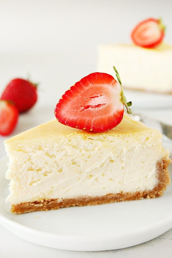 Cheesecake slice with strawberry on top, on white plate.