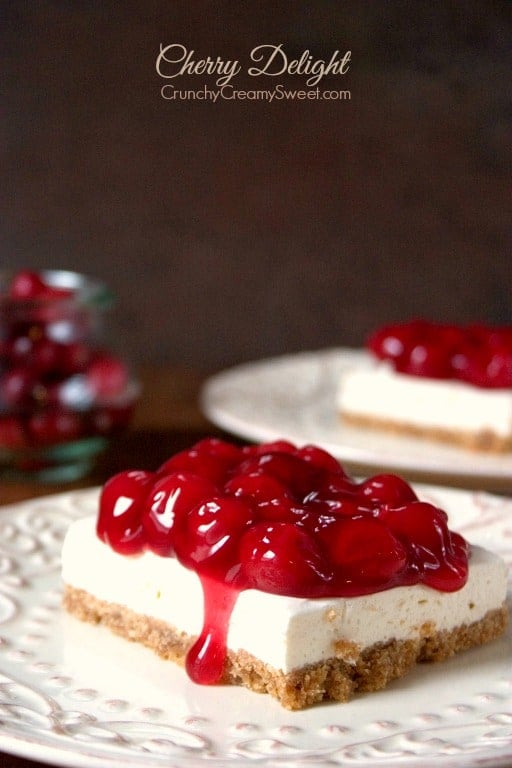 Cherry Delight - a dessert that's always a hit at parties and get-togethers. No-bake cheesecake layer topped with cherry pie filling makes this an irresistible treat! Side shot of square of cherry delight on white plate.