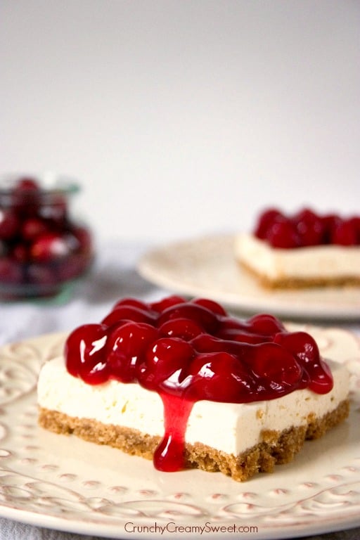 Side shot of cheesecake with cherry pie filling topping on white plate.