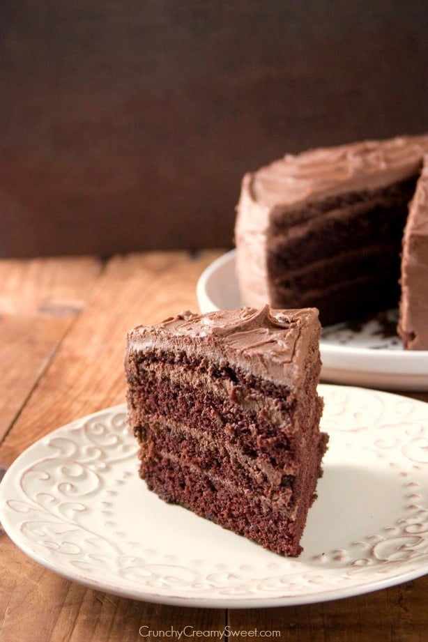 Side shot of a slice of 4 layer chocolate cake with frosting on plate.