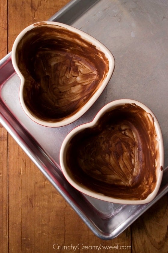Overhead shot of heart shaped ramekins coated with cocoa mixture and set on baking sheet.