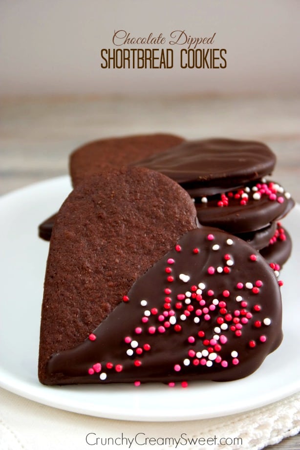 Side shot of chocolate dipped shortbread cookies in heart shapes, on white plate.