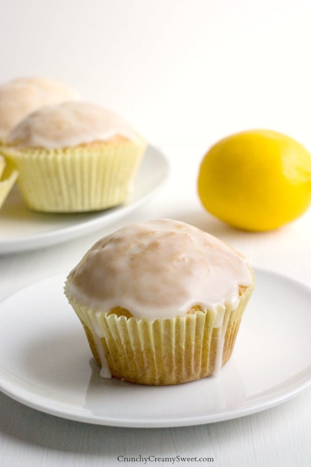 Side shot of a lemon muffin with glaze in yellow cupcake wrapper, on white plate.