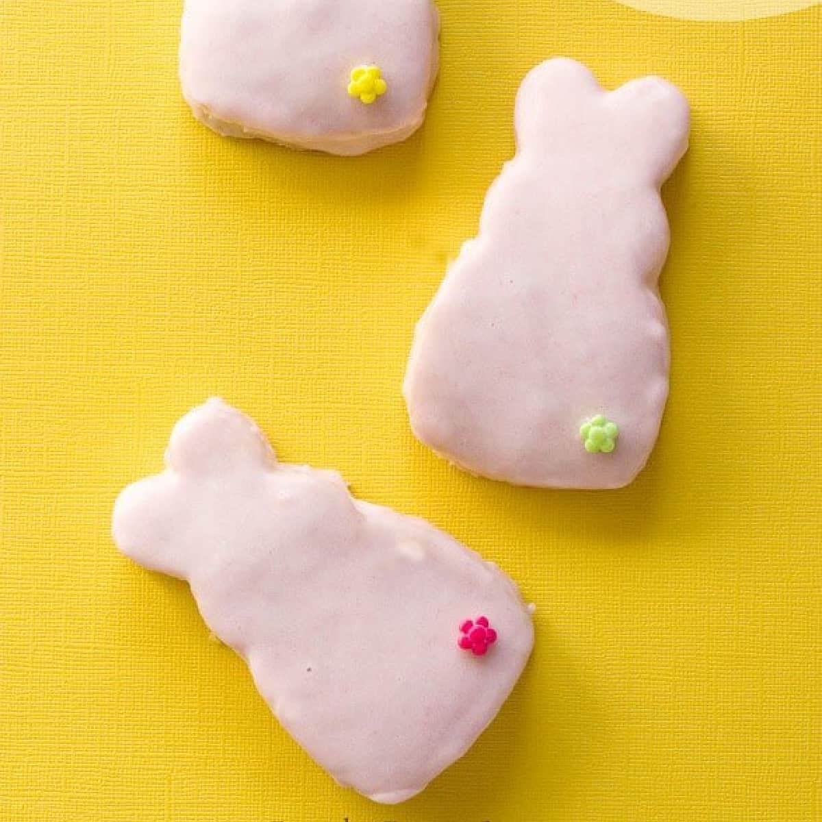 Three cake bunnies covered with pink chocolate on yellow background.