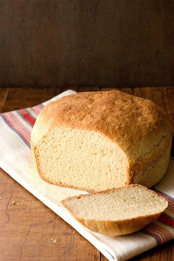 English Muffin Bread - one of the easiest yeast breads you can bake at home! Perfect tender crumb and sturdy crust, this bread is ready for sandwiches! English Muffin Bread on kitchen towel, with one slice cut.