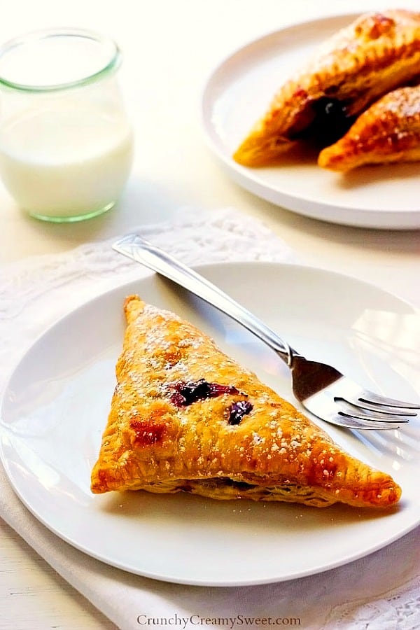 Blueberry Turnovers - easy brunch dessert idea that everyone will love! Flaky, crispy pastry filled with blueberries and creamy lemon filling. Turnover pastry on white plate with fork.