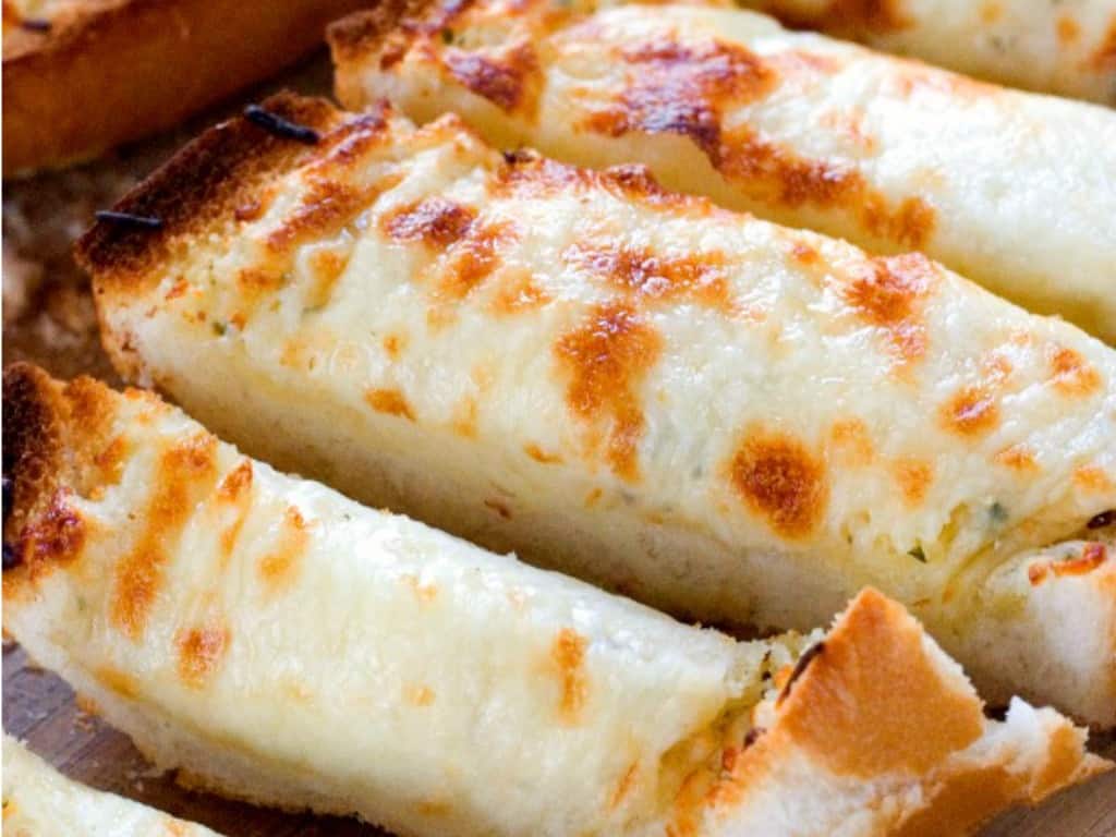 Close up shot of sliced cheesy garlic bread on wooden cutting board.