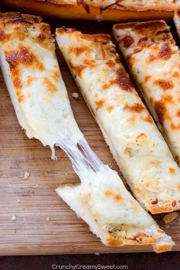 Overhead shot of three sliced of cheesy garlic bread, one pulled apart with gooey cheese.