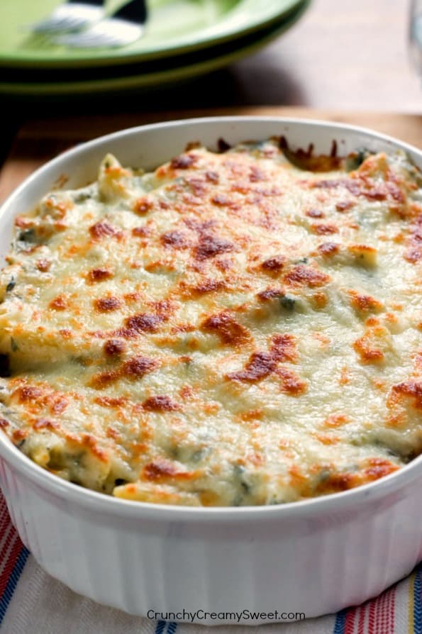 Side shot of spinach pasta with cheesy topping in oval white baking dish.