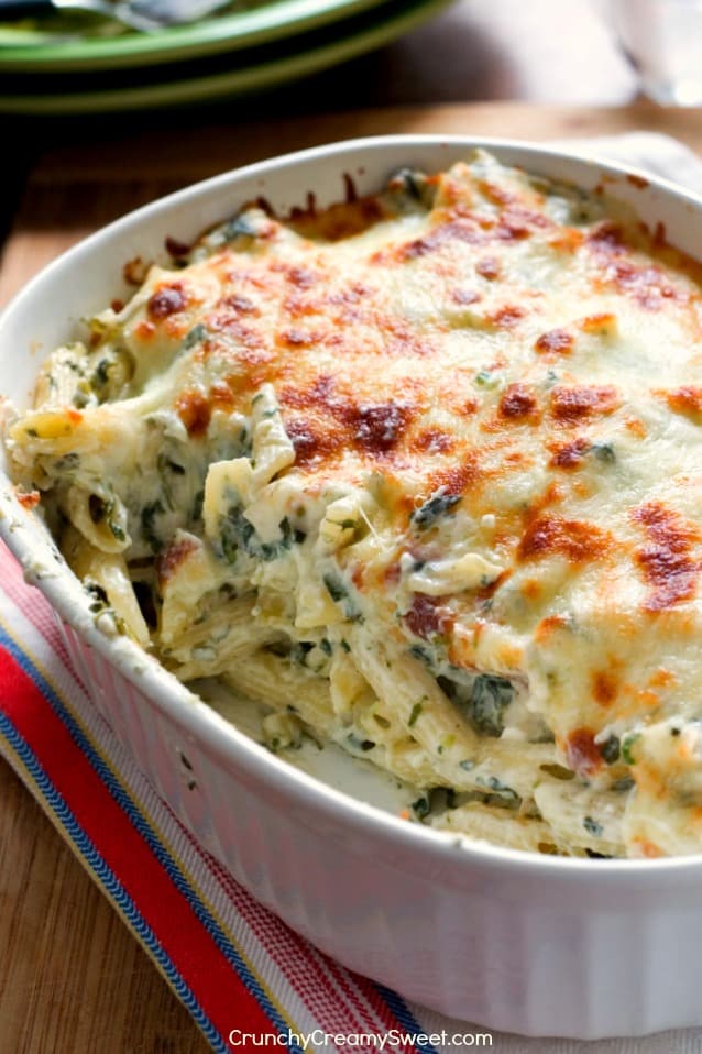 Side shot of pasta with spinach and toasted cheesy top with a serving missing.