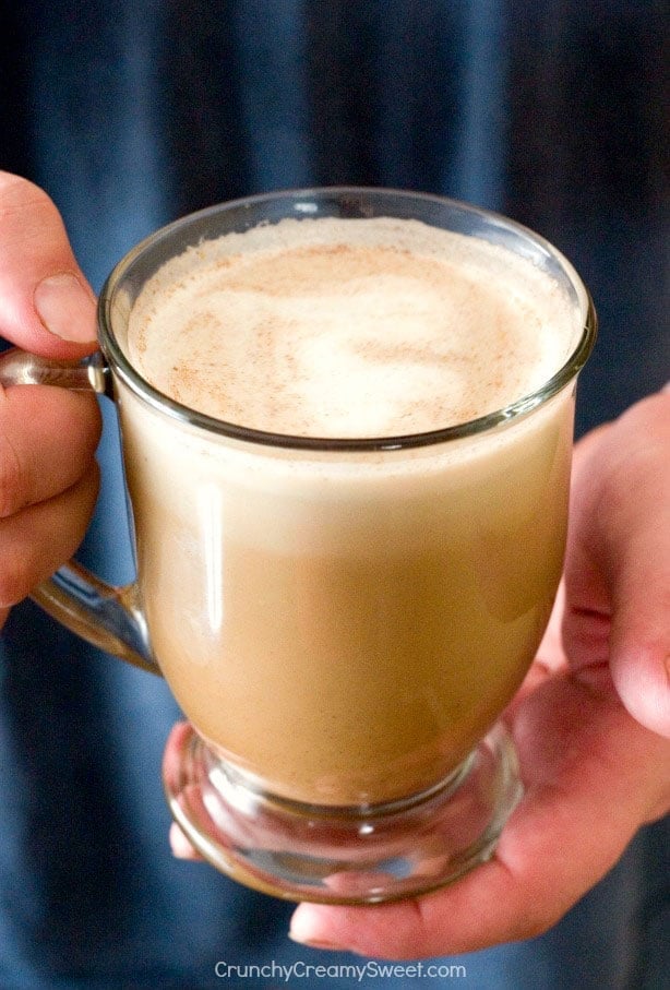 Side shot of pumpkin spice coffee creamer in glass mug, in a man's hands.