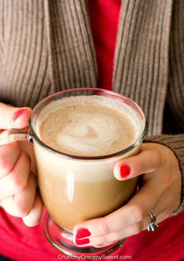 Pumpkin spice latte in glass mug in woman's hands.