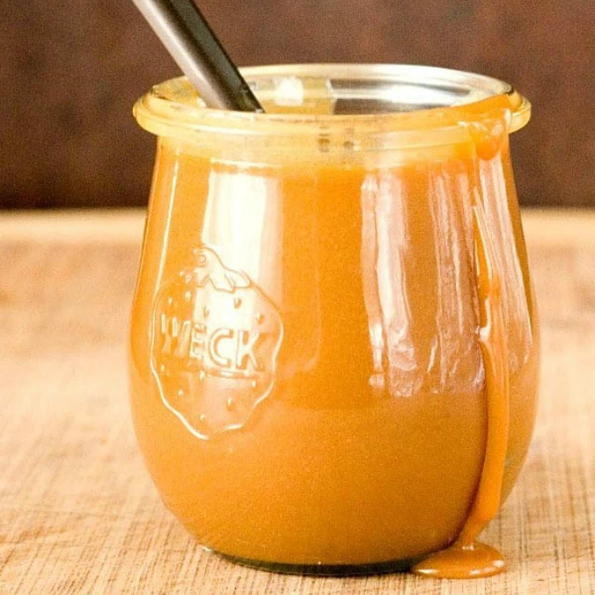 Caramel sauce in a Weck glass jar with a spoon inside, sitting on a wooden cutting board.