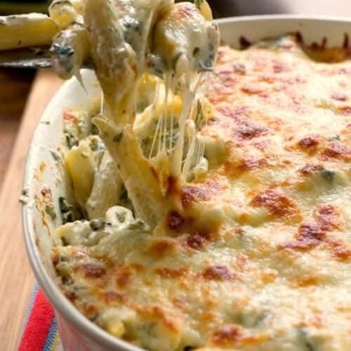 Square image of pasta casserole with spinach in an oval dish.