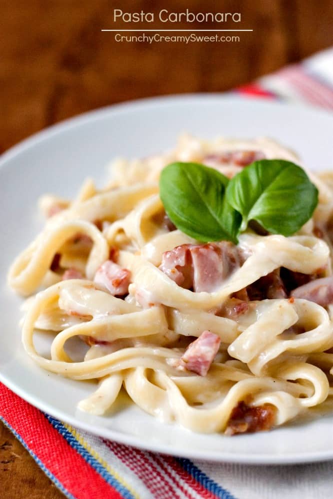 Side shot of pasta carbonara with ham on white plate.