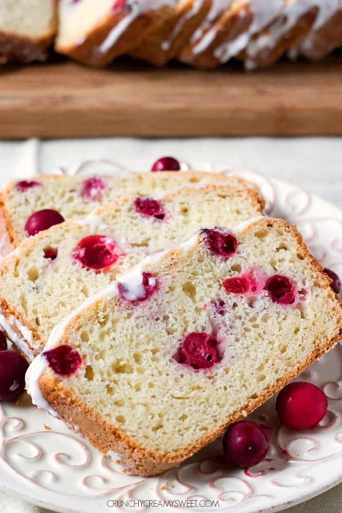 Side shot of slices of cranberry bread on white plate, with the whole loaf in the background.