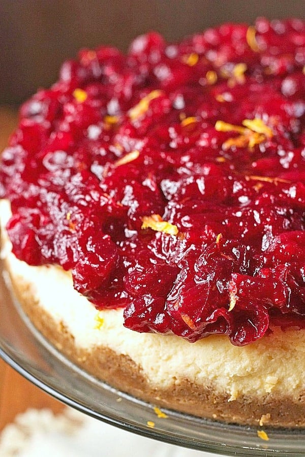 Cranberry Orange Cheesecake - sweet and creamy orange cheesecake baked to perfection, topped with gorgeous cranberry sauce. This cheesecake is perfect finish to your Christmas dinner! Cranberry Orange Cheesecake on a cake stand.