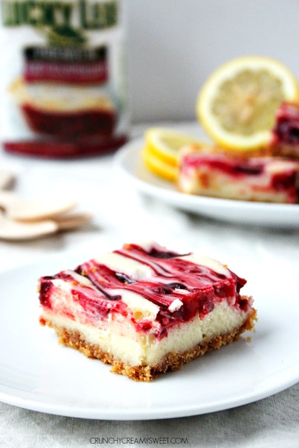 One piece of lemon raspberry cheesecake bars on white plate, with more bars on another plate in background.