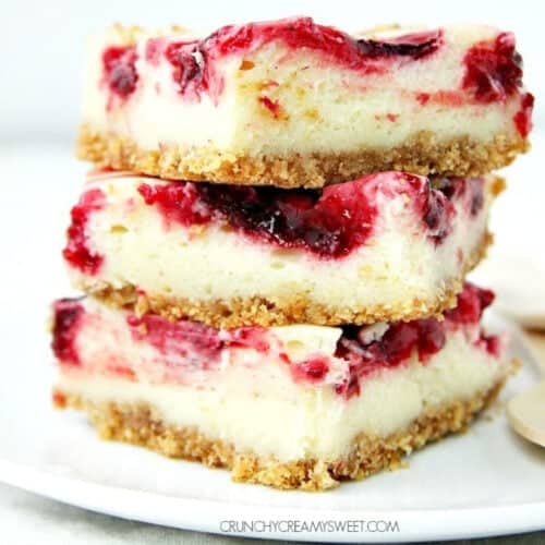 Square image of cheesecake bars with raspberry pie filling, stacked on a white plate.