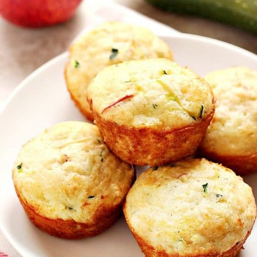 Five muffins with zucchini and apples on white plate.