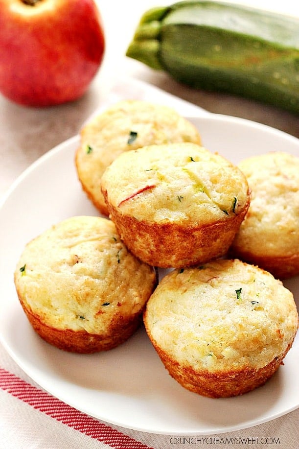 Five muffins with zucchini and apples on white plate.