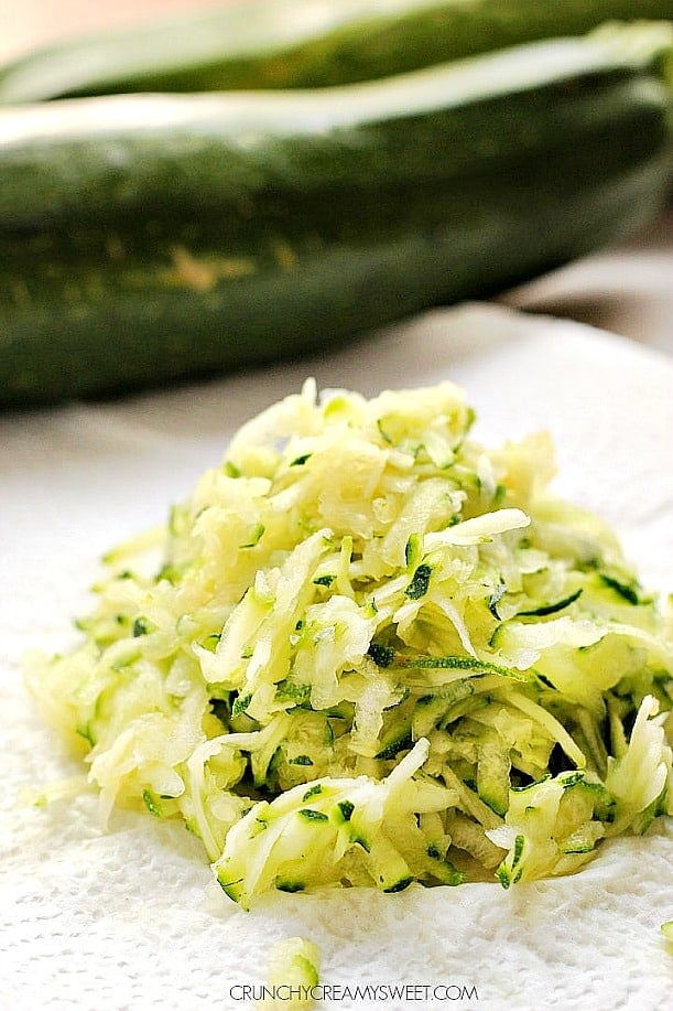 Grated zucchini on paper towel, whole zucchini in background.