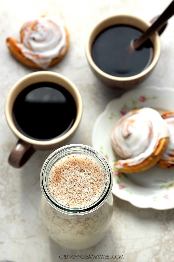 Homemade Cinnamon Roll Coffee Creamer - a 5-minute coffee creamer that requires only 5 ingredients and tastes exactly like your favorite cinnamon rolls! Your mornings deserve to be a little sweeter! Overhead shot of homemade coffee creamer in tall glass bottle and coffee in coffee cups.