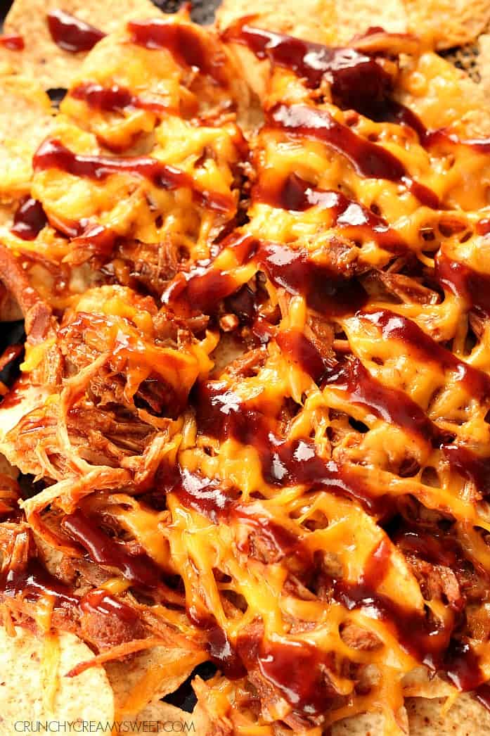 Pulled Pork Nachos - crispy tortilla chips, smoky, sweet pulled pork, melted cheddar and a drizzle of your favorite BBQ sauce - this appetizer will rock your world! Pulled Pork Nachos with melted cheese and BBQ sauce on baking sheet.