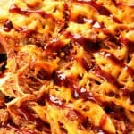 Pulled Pork Nachos with cheese and BBQ sauce on baking sheet.