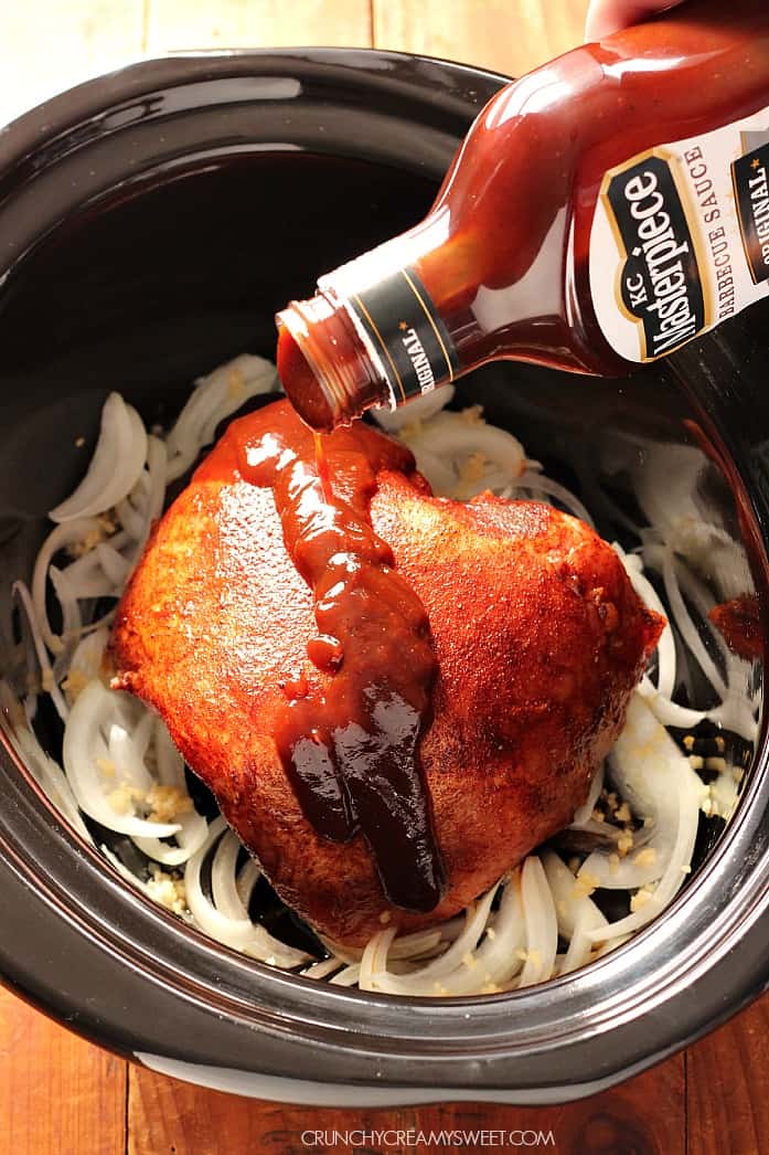 Overhead shot of BBQ sauce being poured over pork roast in slow cooker.