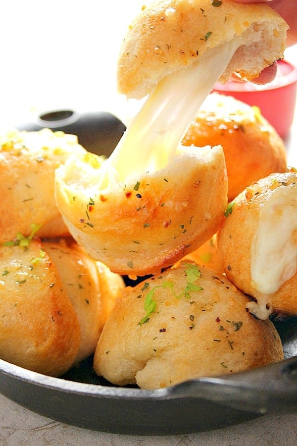 Garlic Cheese Bombs in mini cast iron skillet, one pulled apart with gooey center shown.