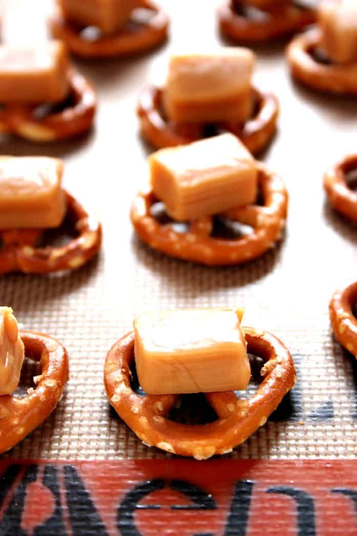 Mini pretzels with a square of caramel on silicone baking mat.
