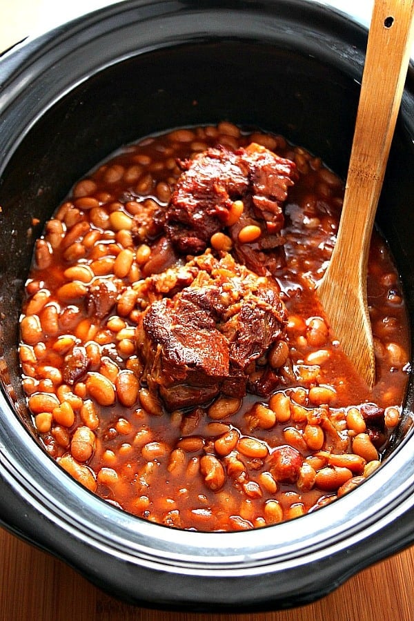 Overhead shot of beans in sauce and meaty ham bone in slow cooker.