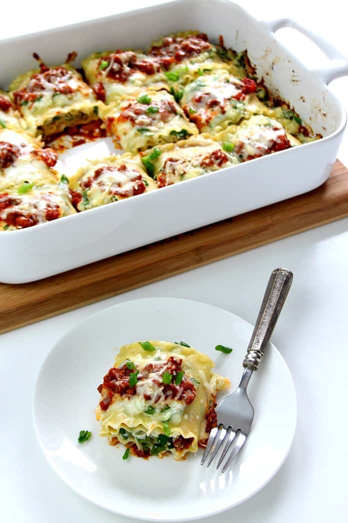 Overhead shot of lasagna roll-ups in baking dish and one on plate with fork.