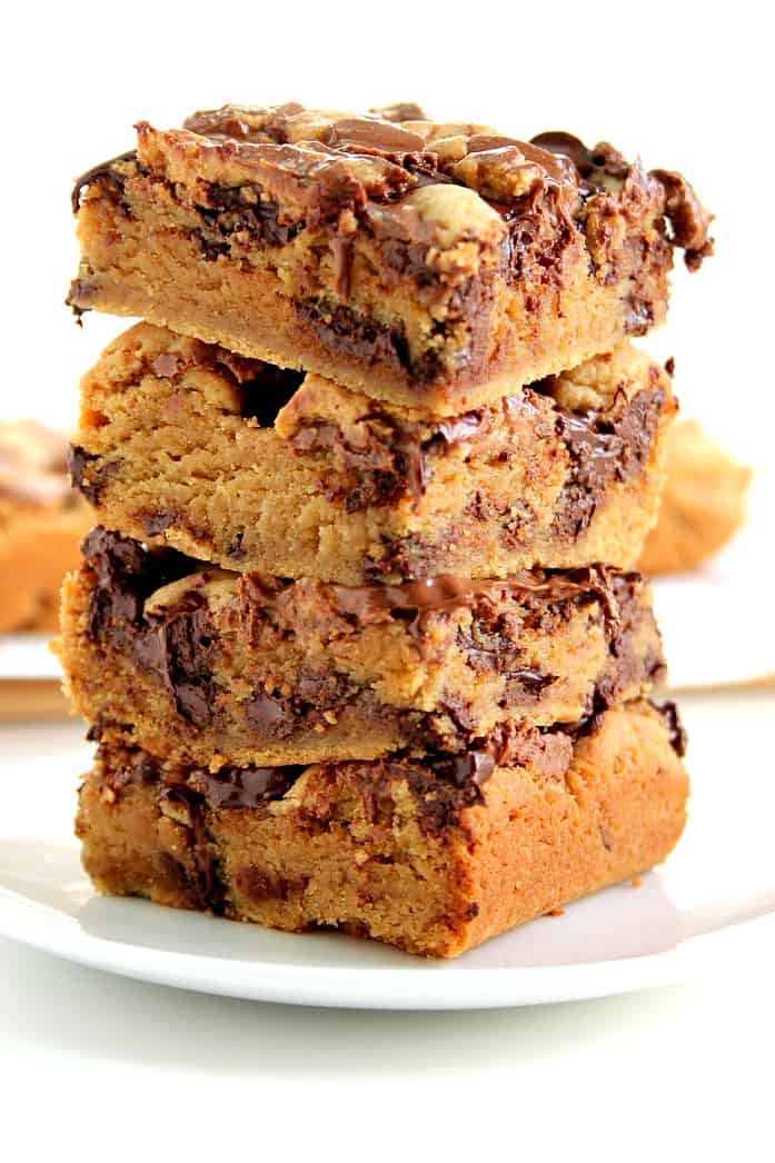 Close up shot of 4 squares of peanut butter cookie bars stacked up on each other on white plate.