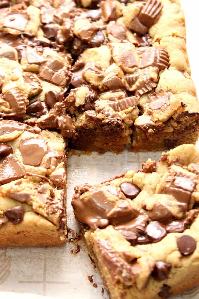 Side shot of peanut butter chocolate cookie bars on parchment paper, one slice cut.