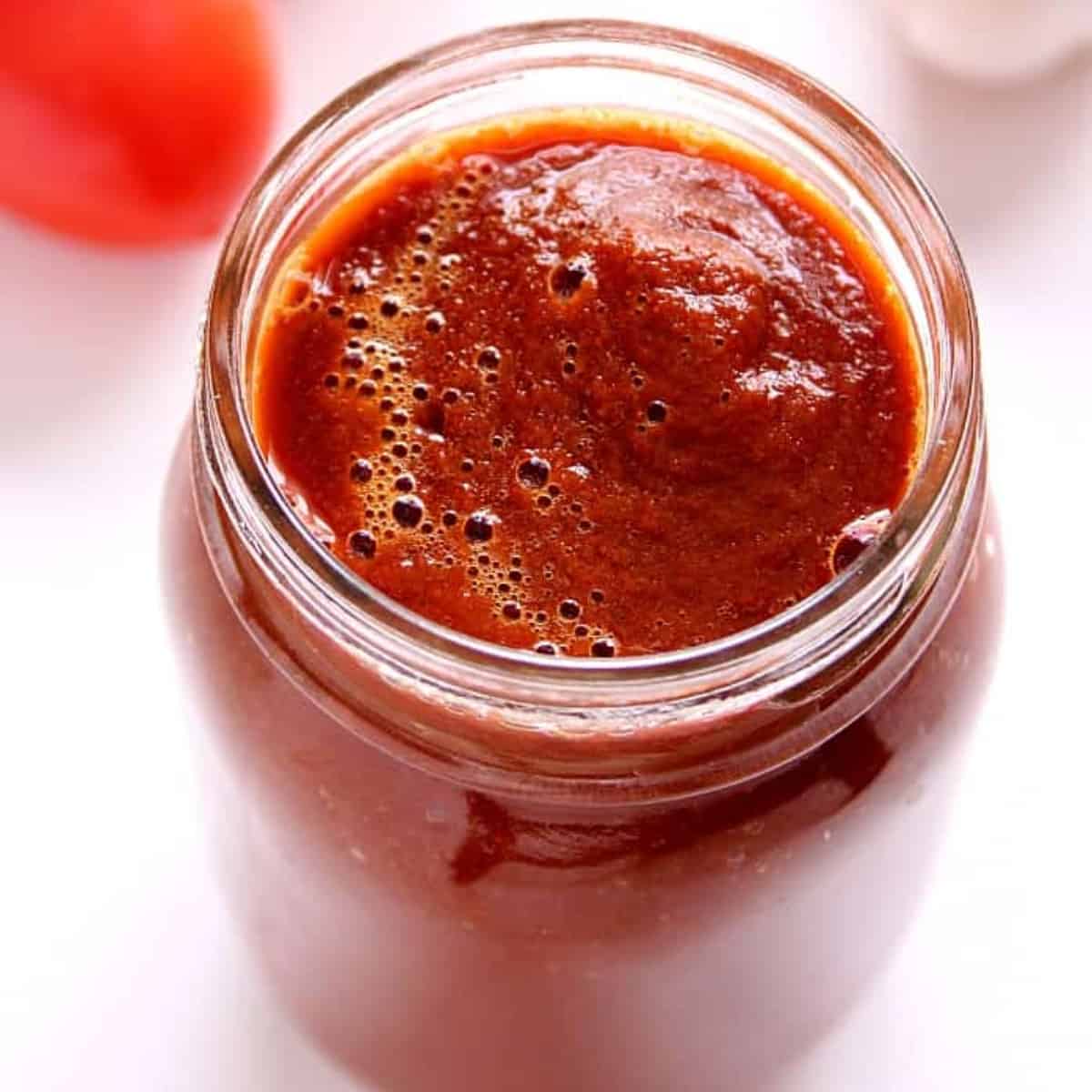 Square image of enchilada sauce in a glass jar.