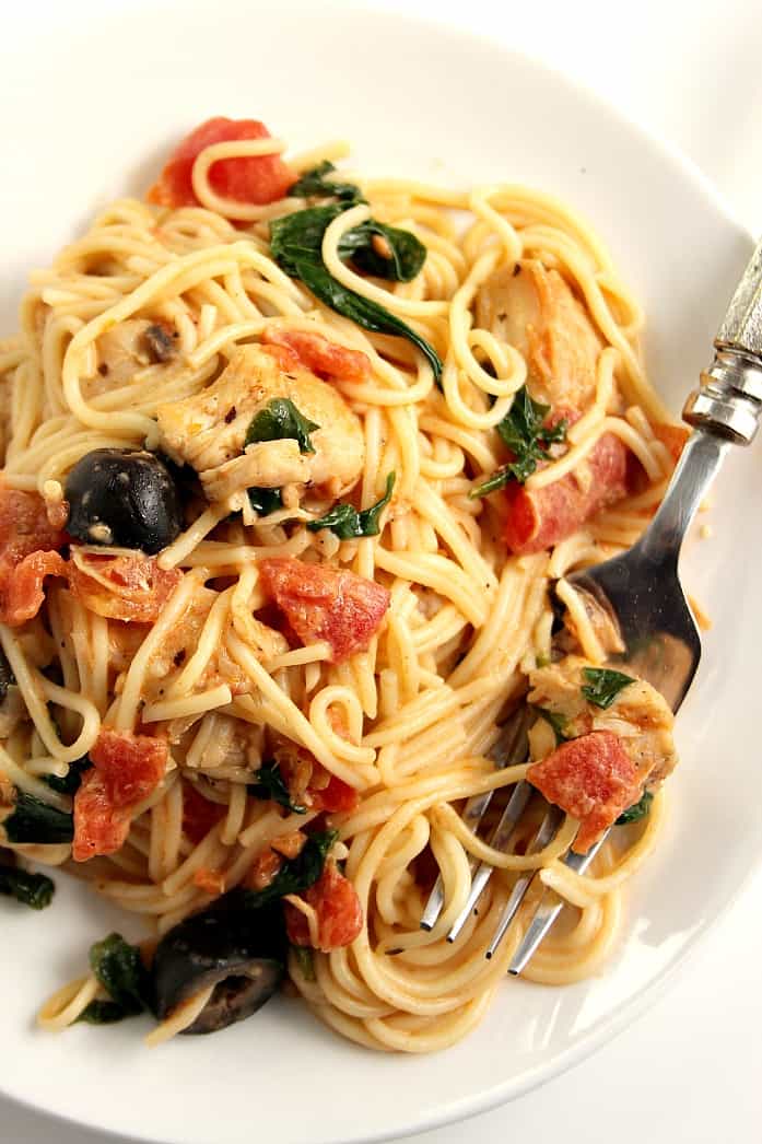 Overhead shot of Angel hair pasta with chicken, tomatoes and olives on white plate. 