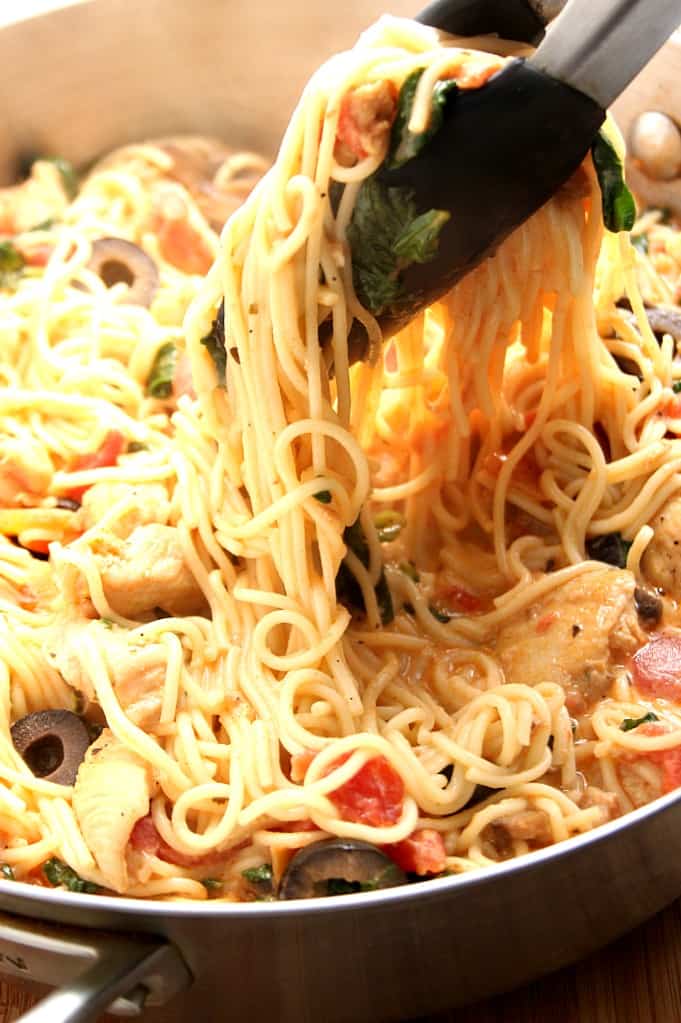 Close up shot of Angel hair pasta in a stainless steel skillet with a bunch of pasta being lifted with kitchen tongs. 