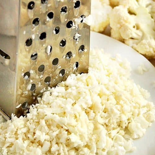 Grater with cauliflower rice on white plate.
