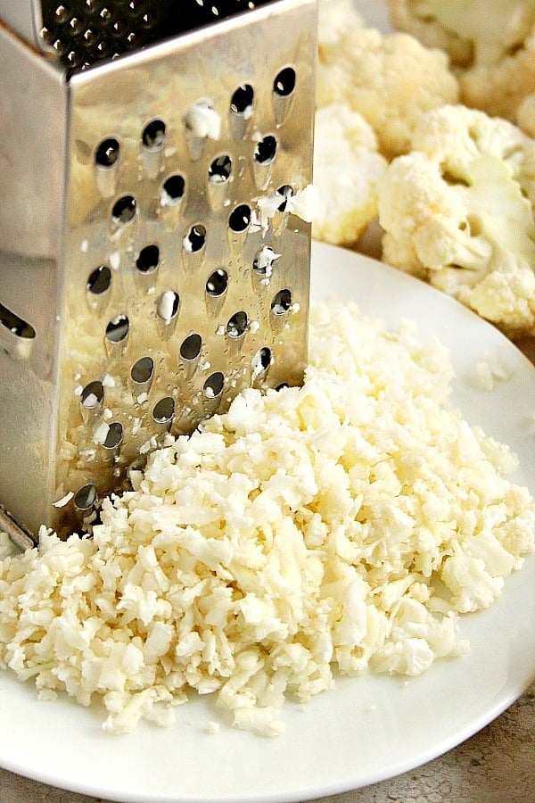 Grated cauliflower with grater in white plate.